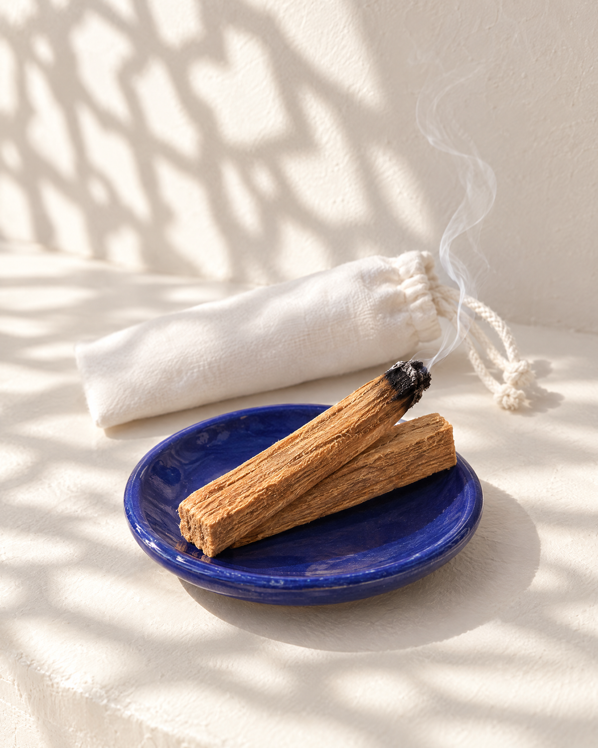 Deux bâtons de palo santo Terre Des Huiles dans une coupelle bleue, avec leur sachet en coton blanc